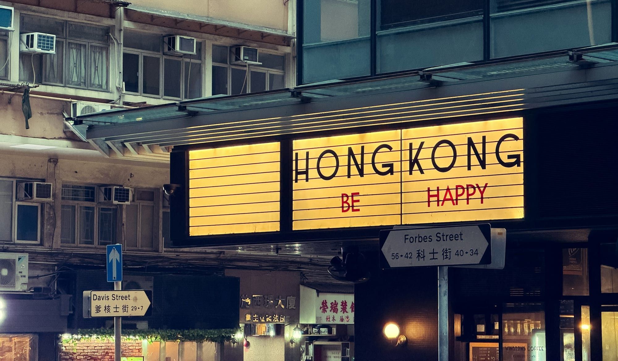 A glowing "Hong Kong, be happy" lightbox sign on Forbes Street, Kennedy Town, at night